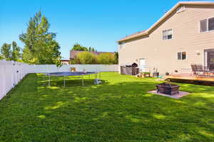 View of yard featuring an outdoor fire pit, a wooden deck, and a trampoline