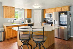 Kitchen featuring appliances with stainless steel finishes, a sink, light countertops, dark wood-type flooring, and a breakfast bar area