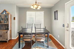 Dining room featuring dark wood-style flooring, baseboards, a chandelier, and plenty of natural light