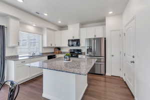Kitchen featuring black appliances, a sink, white cabinetry, a kitchen island, and dark wood-style flooring