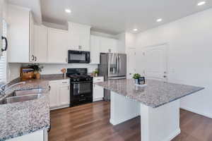 Kitchen featuring black appliances, a sink, dark wood-style floors, a kitchen island, and white cabinets