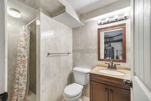 Full bath with water heater, tile walls, a stall shower, vanity, and toilet