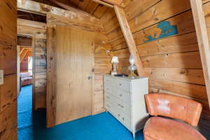 Living area with vaulted ceiling, carpet flooring, wooden walls, and wooden ceiling