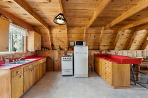 Kitchen with white appliances, a sink, wooden ceiling with exposed beams, wood walls, and a peninsula
