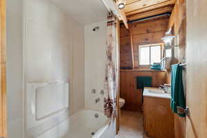Full bathroom with vanity, toilet, shower / bathtub combination with curtain, tile patterned flooring, and wood walls