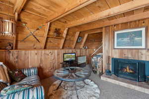 Living room with carpet flooring, wood walls, wooden ceiling, and a fireplace