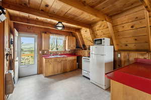 Kitchen with white appliances, heating unit, wooden walls, wood ceiling with exposed beams, and a sink
