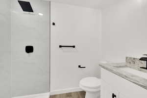 Bathroom featuring tiled shower, vanity, wood finished floors, toilet, and baseboards