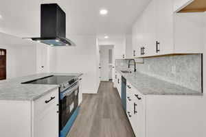 Kitchen with electric stove, island range hood, a sink, light wood finished floors, and recessed lighting