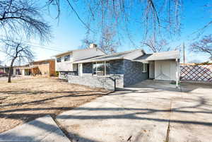 Split level home with a chimney, concrete driveway, a carport, and brick siding