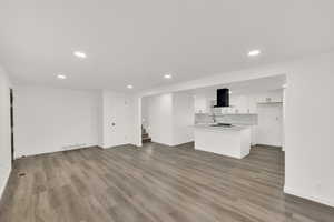 Unfurnished living room featuring baseboards, recessed lighting, stairs, dark wood-style flooring, and a sink