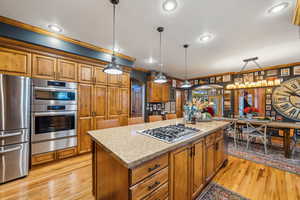 Kitchen with appliances with stainless steel finishes, a warming drawer, brown cabinetry, arched walkways, and a kitchen island