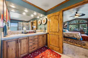 Ensuite bathroom with double vanity, a stall shower, ornamental molding, ceiling fan, and vaulted ceiling