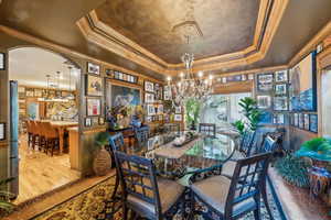 Dining area with a raised ceiling, a chandelier, ornamental molding, wood finished floors, and arched walkways