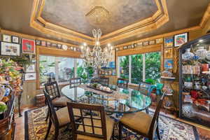 Dining area featuring a raised ceiling, healthy amount of natural light, a chandelier, and crown molding