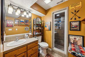 Bathroom with toilet, vanity, tile patterned flooring, a shower stall, and a textured ceiling
