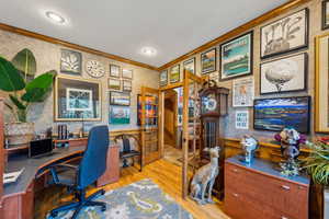 Home office featuring crown molding, wallpapered walls, wood finished floors, and a wainscoted wall