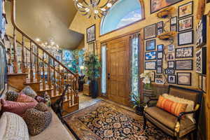 Foyer entrance featuring a chandelier, a towering ceiling, plenty of natural light, stone tile flooring, and stairs