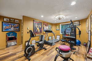 Workout area featuring wood finished floors, a textured ceiling, baseboards, and recessed lighting