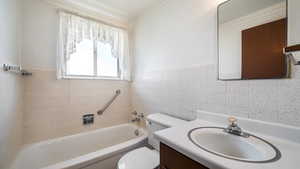 Bathroom with toilet, tile walls, vanity, wainscoting, and bathing tub / shower combination