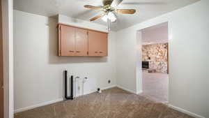Laundry room with cabinet space, hookup for an electric dryer, a ceiling fan, light carpet, and a fireplace