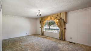 Carpeted empty room featuring a chandelier, a textured ceiling, and baseboards