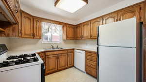 Kitchen with white appliances, brown cabinetry, a sink, light countertops, and light flooring