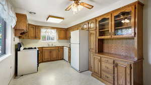 Kitchen featuring white appliances, brown cabinetry, ceiling fan, light floors, and glass insert cabinets
