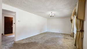 Spare room with a chandelier, light carpet, baseboards, and a textured ceiling