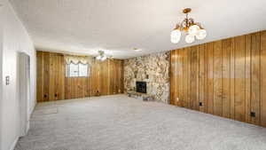 Unfurnished living room featuring wood walls, a textured ceiling, carpet, a fireplace, and a heating unit