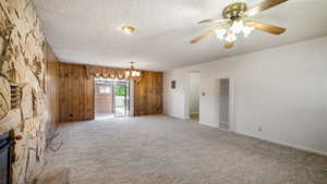 Unfurnished living room featuring a heating unit, a textured ceiling, wood walls, carpet, and a ceiling fan