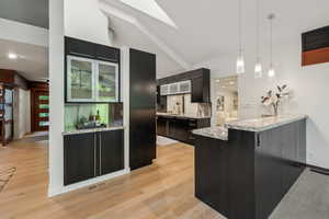 Kitchen featuring hanging light fixtures, a peninsula, light wood-type flooring, glass insert cabinets, and dark cabinetry