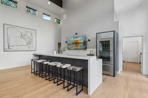 Indoor bar featuring a high ceiling, built in fridge, light wood-type flooring, and baseboards
