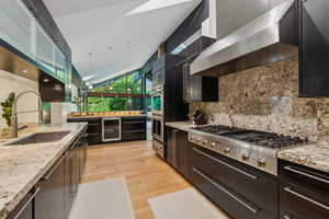 Kitchen featuring wall chimney exhaust hood, beverage cooler, a sink, appliances with stainless steel finishes, and tasteful backsplash