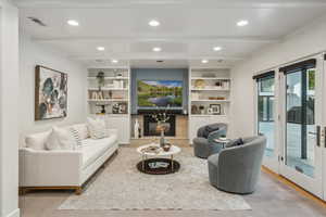 Living area with beamed ceiling, wood finished floors, recessed lighting, and built in shelves