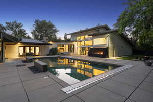 Back of property featuring a patio, an outdoor pool, an outdoor fire pit, a lit fireplace, and a chimney