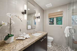 Bathroom featuring tile walls, vanity, a stall shower, and toilet