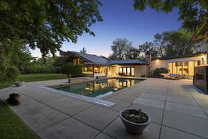 Pool at dusk featuring an outdoor living space, a patio area, an outdoor pool, and a lawn