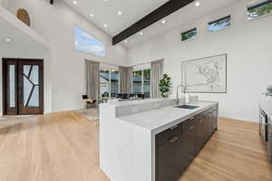 Kitchen featuring a sink, light wood-type flooring, a high ceiling, a center island with sink, and baseboards