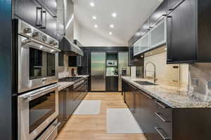Kitchen featuring stainless steel appliances, a sink, light wood-type flooring, lofted ceiling, and backsplash