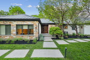View of front of property with a standing seam roof, stone siding, a front yard, and metal roof