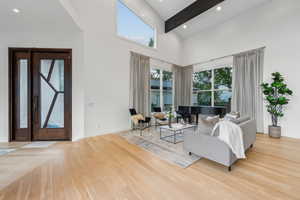 Living room with wood finished floors, a towering ceiling, baseboards, beam ceiling, and recessed lighting