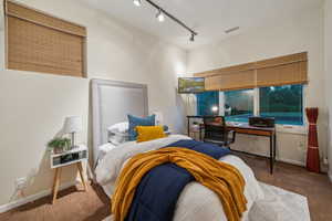 Carpeted bedroom featuring rail lighting, baseboards, and an office area