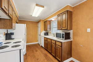 Kitchen with white appliances, a sink, brown cabinets, light wood-type flooring, and baseboards