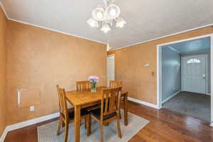 Dining area featuring hardwood / wood-style flooring, a chandelier, baseboards, ornamental molding, and a textured ceiling