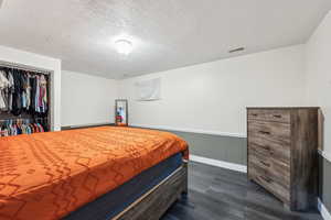 Bedroom with dark wood finished floors, a wainscoted wall, a textured ceiling, a closet, and baseboards