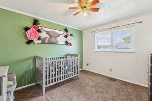 Bedroom featuring a textured ceiling, a crib, crown molding, carpet floors, and baseboards