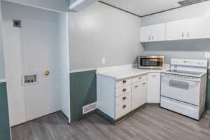 Kitchen featuring white range with electric stovetop, stainless steel microwave, wood finished floors, light countertops, and white cabinets