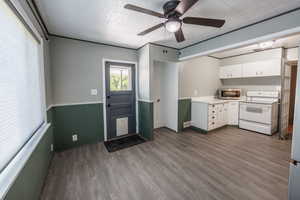 Kitchen with electric range, stainless steel microwave, wood finished floors, light countertops, and white cabinetry