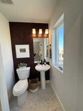 Bathroom with baseboards, toilet, speckled floor, and an accent wall
